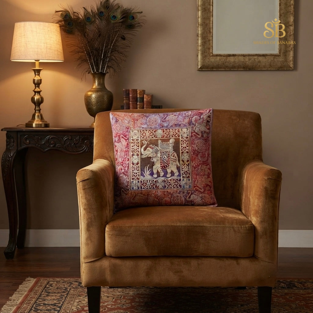 Pink brocade Banarasi cushion cover with caparisoned elephant motif on a tan velvet armchair