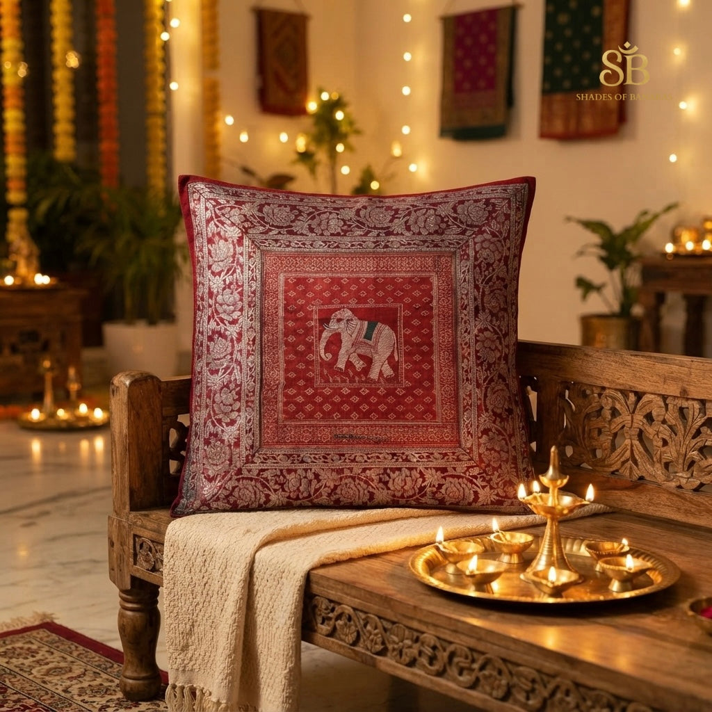 Red brocade Banarasi cushion cover with elephant motif on a carved wood bench with diyas