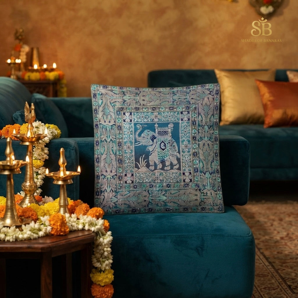 Teal blue brocade Banarasi cushion cover with elephant motif beside brass diyas