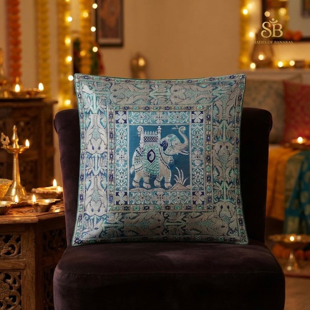 Teal blue brocade Banarasi cushion cover with elephant motif beside festive brass diyas